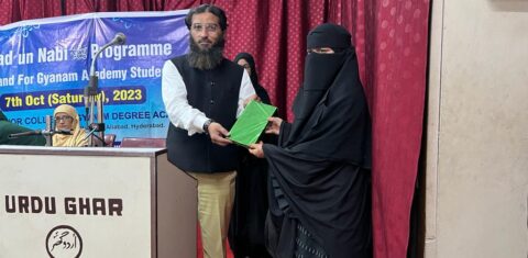 A presenter handing an award to a student during the Milad-un-Nabi ﷺ event at Gyanam Junior College."