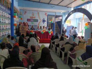 Flag hoisting ceremony at Gyanam Junior College on Independence Day with students performing cultural programs in the background.