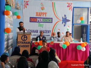 Flag hoisting ceremony at Gyanam Junior College on Independence Day with students performing cultural programs in the background.