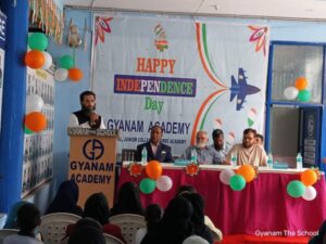 Flag hoisting ceremony at Gyanam Junior College on Independence Day with students performing cultural programs in the background.