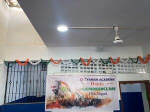 Flag hoisting ceremony at Gyanam Junior College on Independence Day with students performing cultural programs in the background.